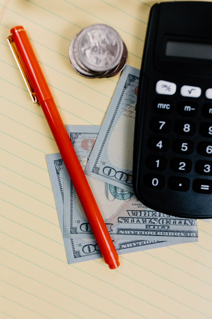 Close-up of a pen, calculator, and cash on a notepad, representing financial planning.